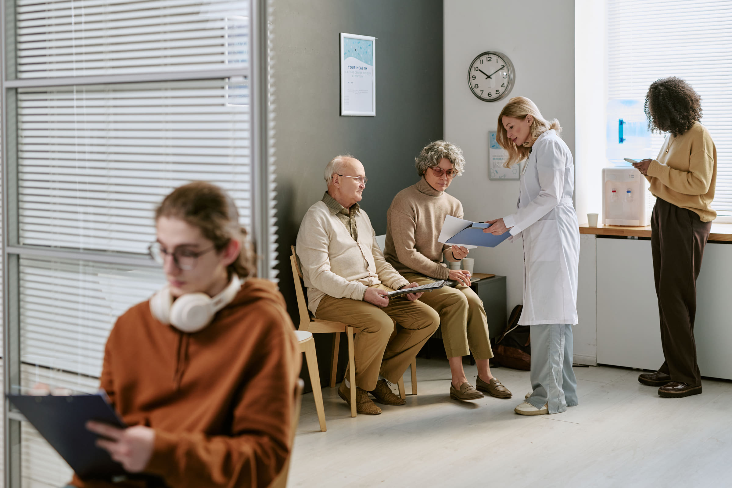 Patients waiting in a clinic reception area while a clinician speaks with one of them